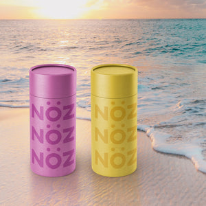 Colorful bottles of eco friendly sunscreen sitting on the beach with a sunset in background 